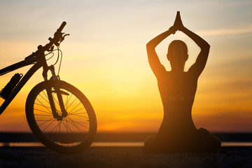 Sports woman doing yoga at sunrise on the sea beach against the background of orange sky and...