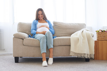 Obraz premium Pregnant woman sitting on sofa in casual comfortable clothes