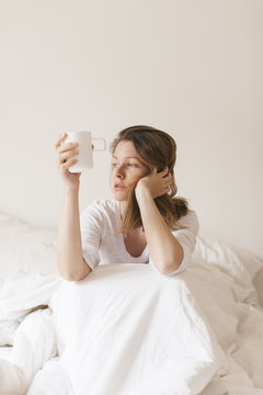 Woman in white bed drinking coffee