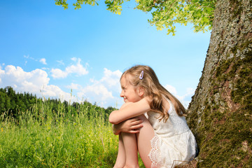 Naklejka na ściany i meble young girl sit next to a tree and smile into the summer sun. she plays with electronic devices, red apple, flowers. sky is blue and the grass is green.