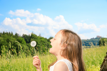 young girl sit next to a tree and smile into the summer sun. she plays with electronic devices, red apple, flowers. sky is blue and the grass is green.