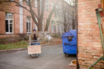 Homeless beggar with stolen shopping cart with board need money on it. View of a homeless man...