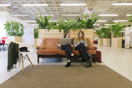 Two young women working, sketching and designing. Using a laptop, sitting on a couch.
