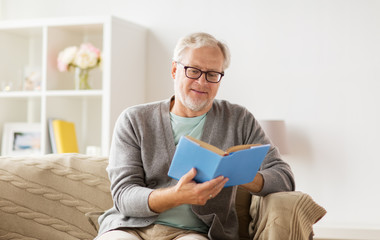 senior man on sofa reading book at home
