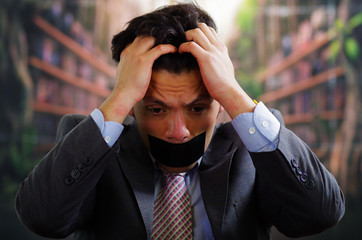 Businessman with a black tape in his mouth, and touching his hair with desperation, in a blurred...