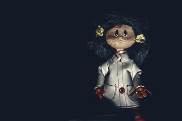 Sinister rag doll with long dark hair and dressing a white leather trench coat and red gloves, in darkness