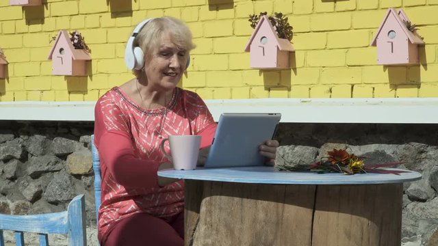 Pretty old woman listens music and uses tablet