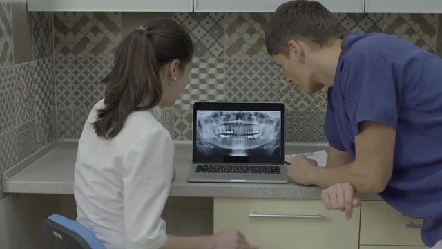 Two doctors analyzing X-ray image of teeth on laptop