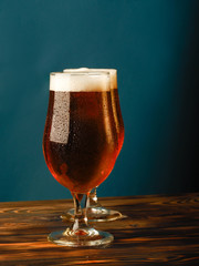 Two glasses with a light beer on a wooden table and blue background.