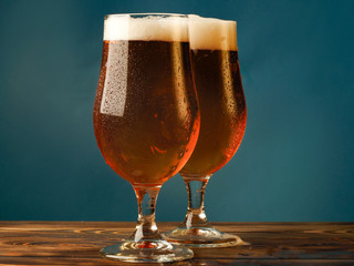 Two glasses with a light beer on a wooden table and blue background.