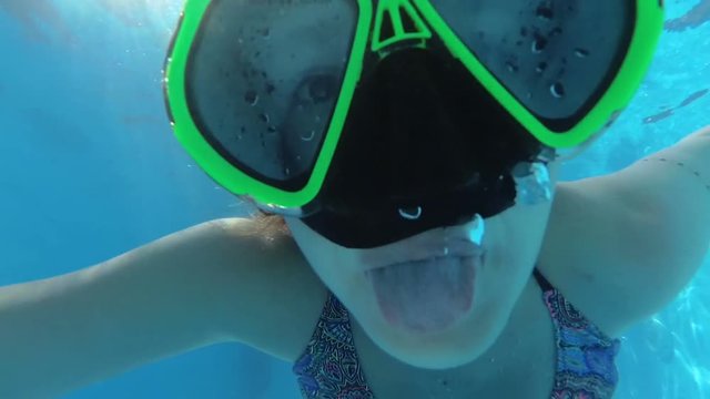 girl in a mask under the water in the swimming pool looks into the camera, bubbles
