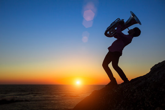 Silhouette of musician play Tuba on sea shore at amazing sunset.