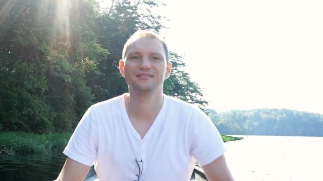 Happy smiling young man rowing boat on lake in Virginia during summer with sun rays behind trees