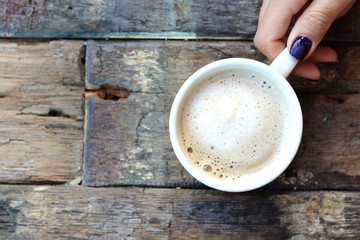 Woman hand with a cup of  coffee or cappuccino above a weathered wooden table 