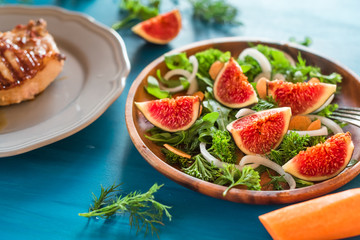 Autumn salad of arugula, figs in a brown earthenware plate on a dark background. top view