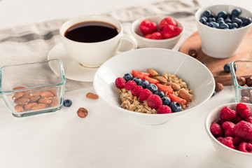 Good morning - healthy breakfast background with oatmeal coffee, berries, egg, nuts. White wooden food background,