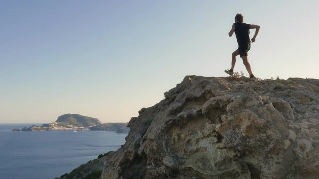 Running man arrives on top of a cliff on an island in front of the ocean
