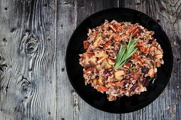 Autumn rice pilaf with apples and cranberries in a black plate against an old wood background