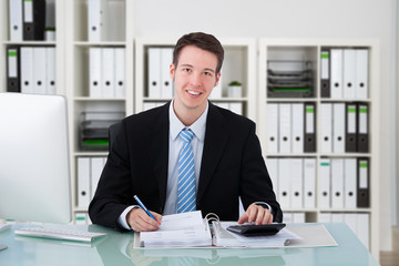 Fototapeta premium Confident Businessman Using Calculator At Office Desk