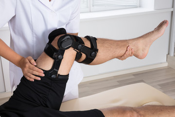 Physiotherapist Fixing Knee Braces On Man's Leg