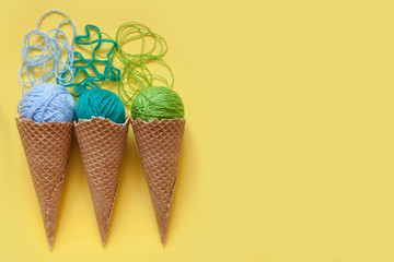 Balls of yarn lie in a waffle cone for ice cream. Coloured wool.