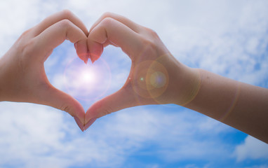 Female hands in heart shape with peaceful sky background.