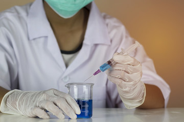 Fototapeta premium The doctor holds a syringe with a blue vaccine inside beaker. Vaccines help build immunity and disease prevention. Laboratory room. Close up and blur.