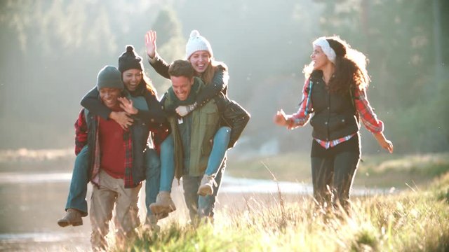 Five friends have fun piggybacking by a rural lake