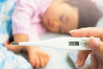 Close-up mother's hand holding thermometer. Taking child's temperature.