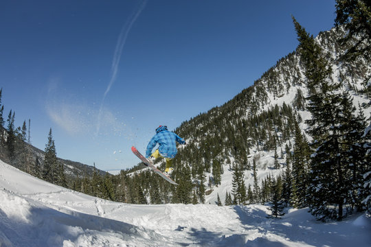 Snowboarder freerider jumping from a snow ramp in the sun on a background of forest and mountains