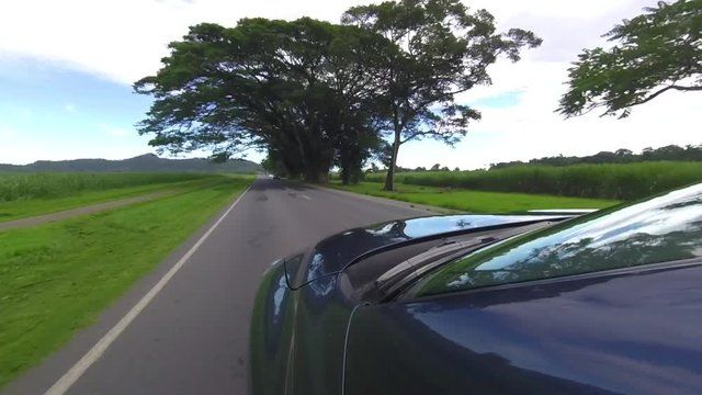 A gopro shot that is mounted on a black car. The car drives past different stores on a developing rural place.