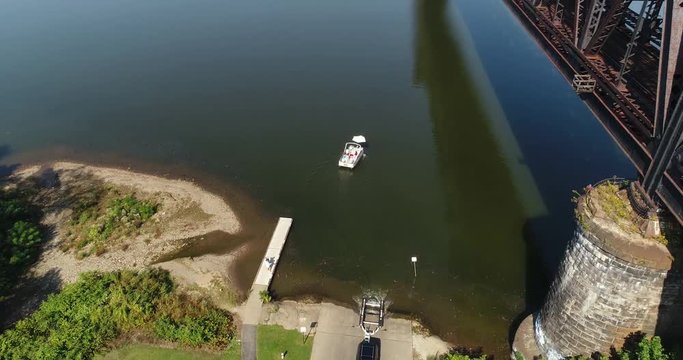 A high angle rising aerial establishing shot of a recreational boat being launched on the Ohio River under a railroad bridge.  	