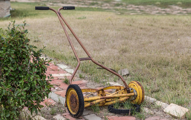 horizontal image of an old vintage antique manual push mower with a broken wheel.