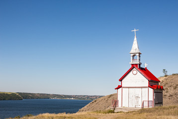Fototapeta na wymiar horizontal image of a quaint little white church with red roof sitting on the side of a hill with the lake down below under a clear blue sky with copy space.