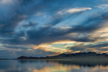 fiery sunset reflecting on mirror water surface of sea with dark fluffy clouds on sky 
