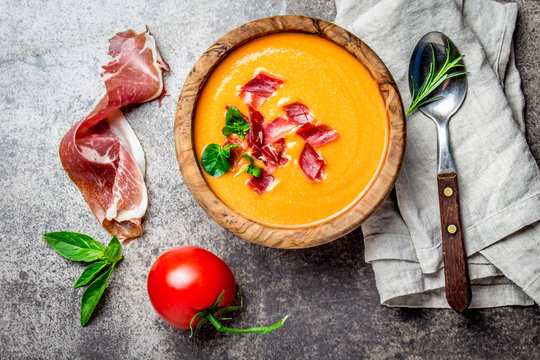 Spanish tomato soup Salmorejo served in olive wooden bowl with ham jamon serrano on stone background. Top view