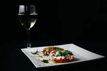 Caprese Salad on a white plate with a glass of white wine, horisontal with dark negative space