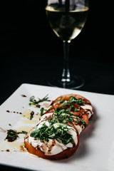 Caprese Salad on a white plate with dark background styled with a glass of white wine