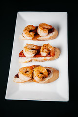 Plate of delicious  bruschetta with grilled shrimp and sausage on dark background