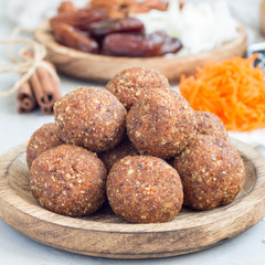 Obraz na płótnie Canvas Healthy homemade paleo energy balls with carrot, nuts, dates and coconut flakes, on wooden plate, square format