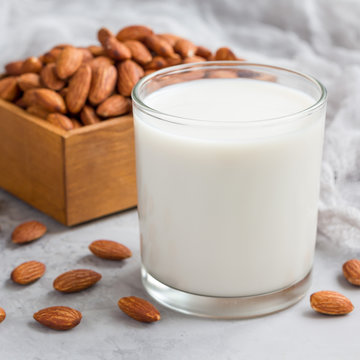 Almond milk in glass with almonds on background, square format