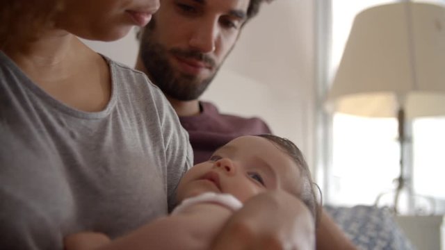 Parents Cuddling Baby Daughter In Bedroom At Home