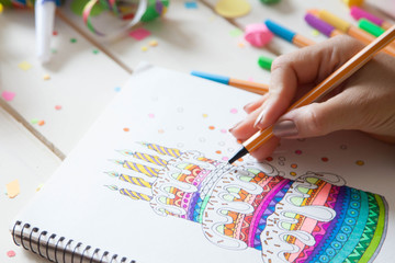 The girl draws a cake with bright colored markers. Gifts, rosettes, confetti and festive...
