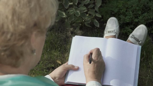 Senior woman paints inside notebook