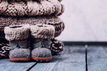 Stack Pile of cozy knitted sweaters and holiday christmas baby toy boots on a wooden table. Warm concept. Copy space