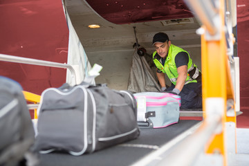 Worker Placing Baggage On Conveyor To Unload Airplane