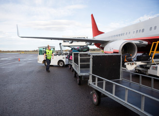 Worker Walking By Luggage Trailers On Runway