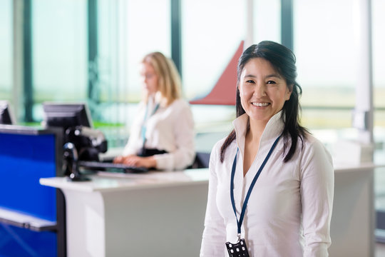 Ground Staff Smiling While Colleague Working At Airport Receptio