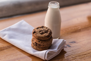 Stack of chocolate chips cookies and a bottle of milk on wooden background