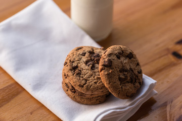 Stack of chocolate chips cookies and a bottle of milk on wooden background